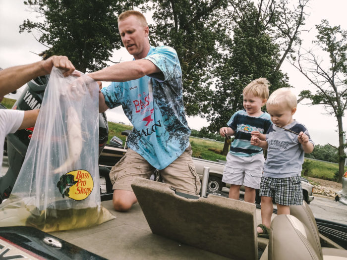 Andrew buss and 2 children on a boat putting a fish in a clear plastic bag filled with water on a fishing trip
