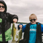 Two young boys on a boat holding up 4 fish