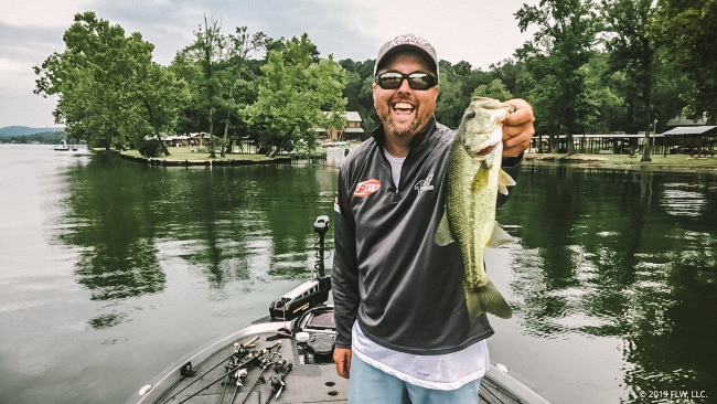 Ron Nelson holding up a bass while standing on the deck of his boat.