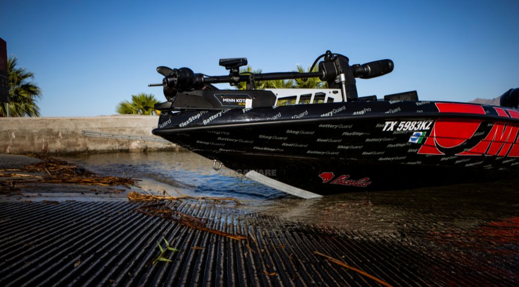 Black boat with a red logo and a gray Megaware KeelGuard keel protector beached on a concrete ramp.